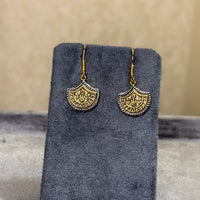 A pair of gold-toned dangle earrings with ornate circular cutout details, displayed on a dark gray velvet jewelry card against a neutral gray background.